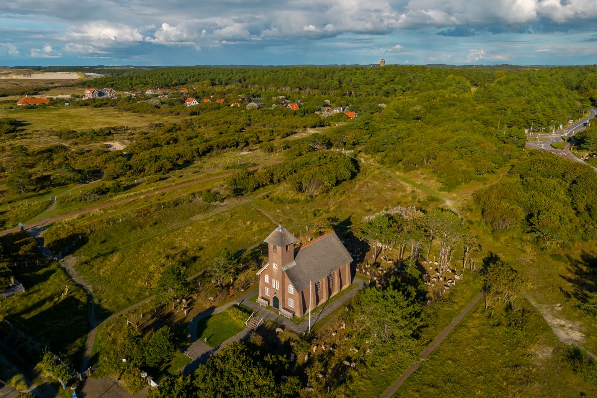 Bovenaanzicht/luchtfoto van het Vredeskerkje in Bergen aan Zee met daaromheen het groene landschap, het bos en de duinen